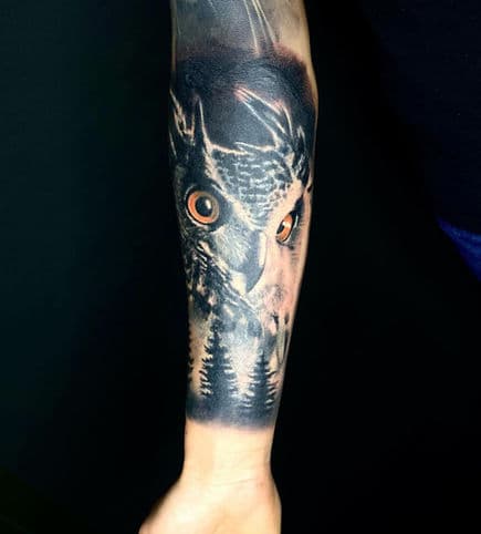 Realistische uil met oranje ogen en boslandschap op onderarm.