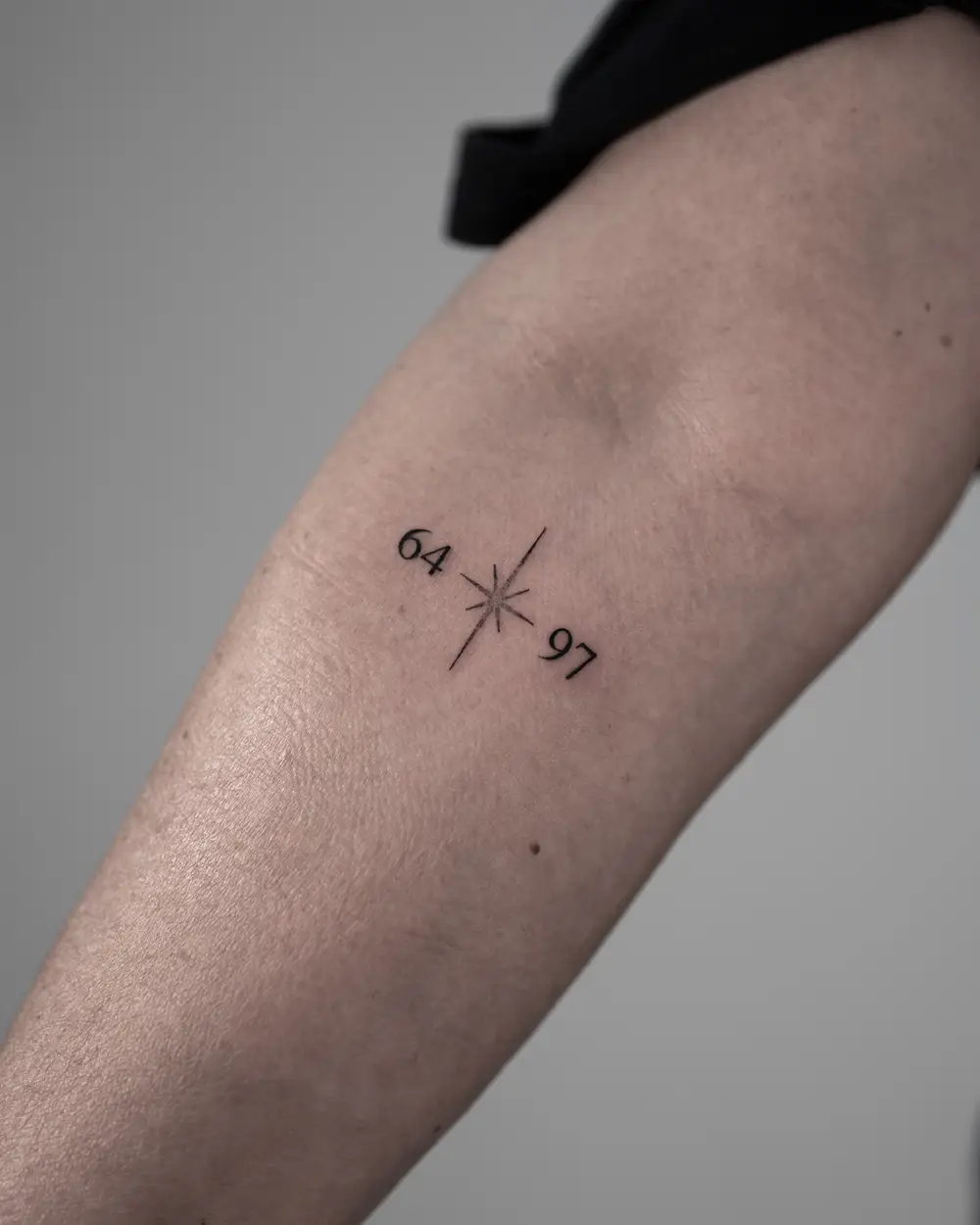 Minimalistische fineline tattoo met '64', een ster en '97' op de onderarm.
