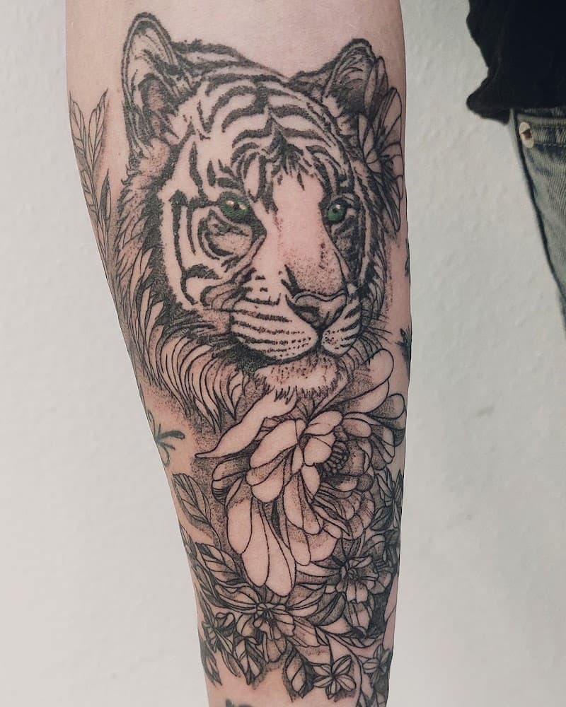 Zwart-grijze tijger met groene ogen en bloemen op onderarm.