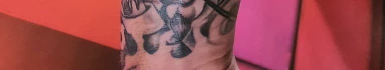 Zwart-wit tattoo van een schedel of demon op de onderarm.