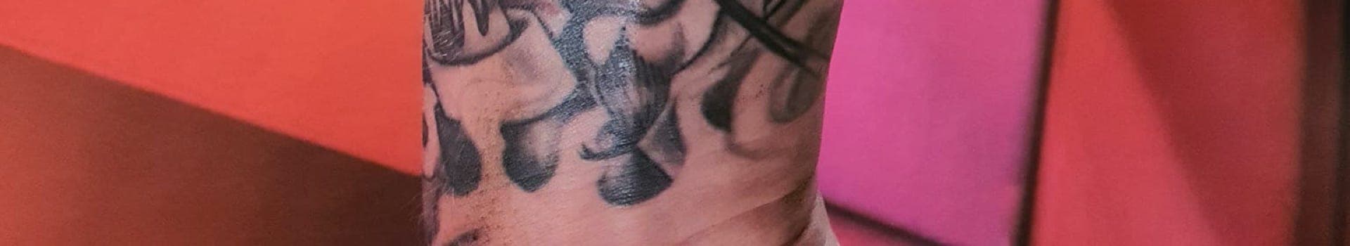 Zwart-wit tattoo van een schedel met een hoed en rook op de onderarm.