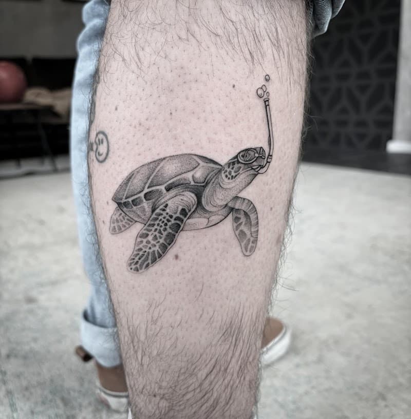 Zwart-wit tattoo van een schildpad met een snorkel op het onderbeen.