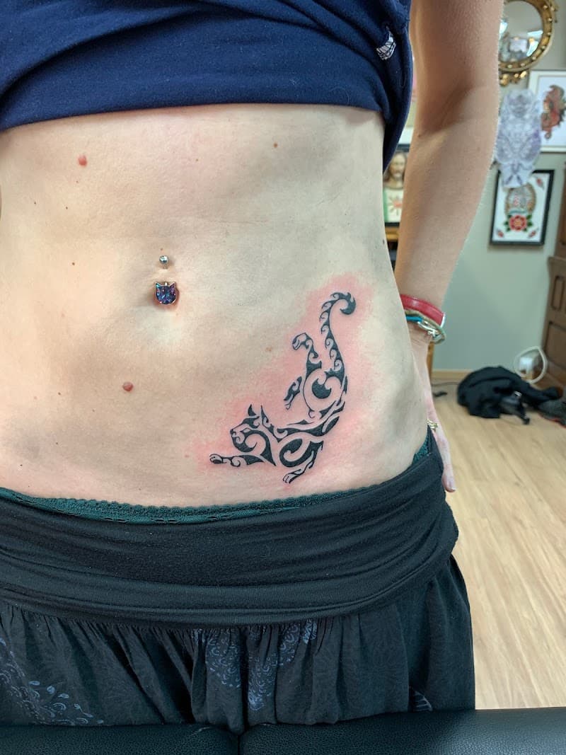 Zwarte tribal kat tattoo op de heup/buik.