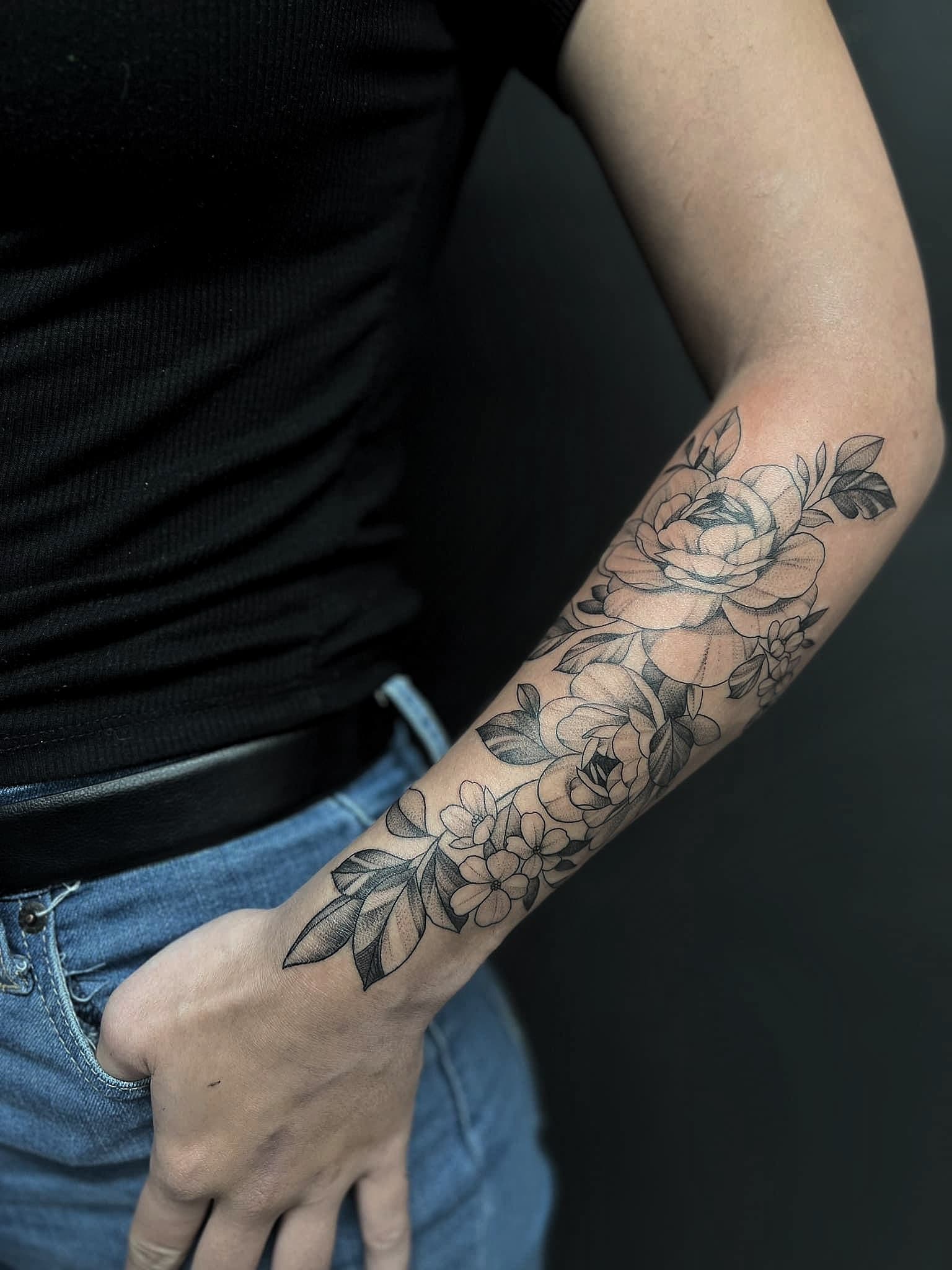 Gedetailleerde zwart-wit bloemen tattoo op de onderarm.