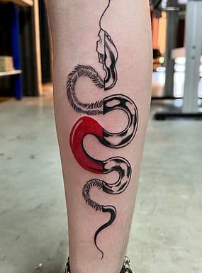 Abstracte slang tattoo met rode en zwart-witte segmenten op onderbeen.