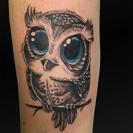Schattige cartoon uil tattoo met grote blauwe ogen op onderbeen.