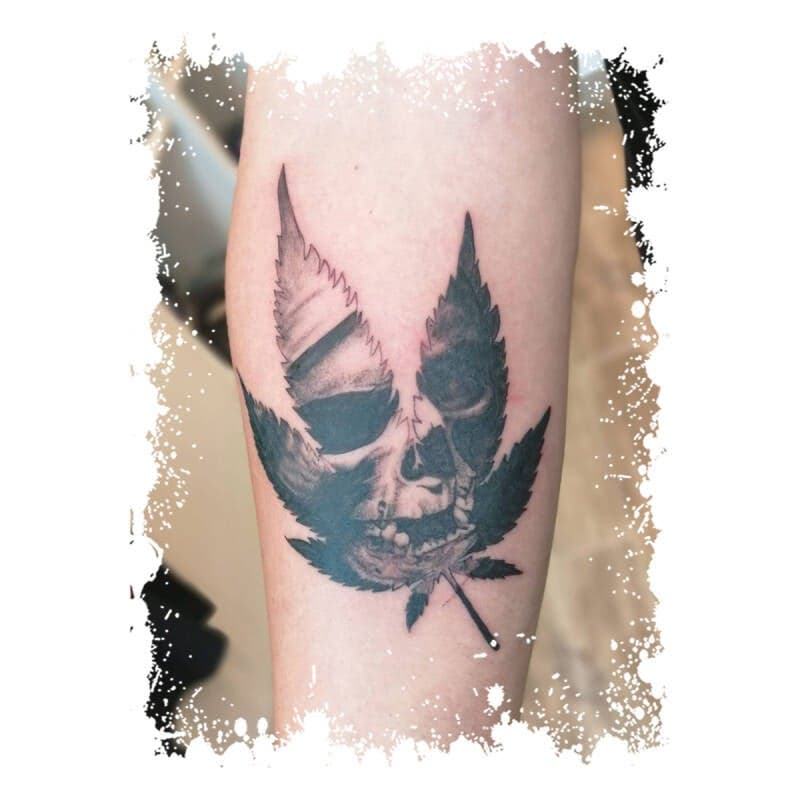 Zwart-wit tattoo van een schedel in een wietblad op de onderarm.
