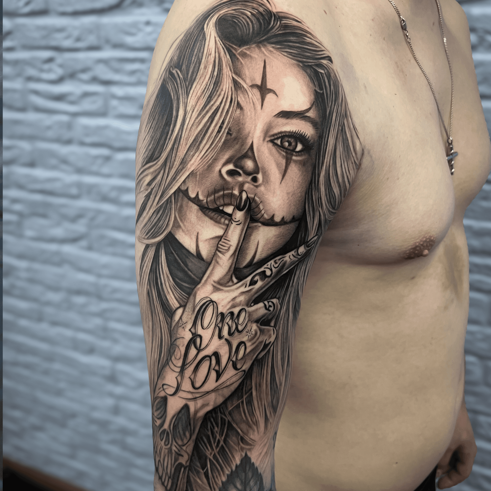 Realistisch portret van een vrouw met 'One Love' handgebaar op bovenarm.