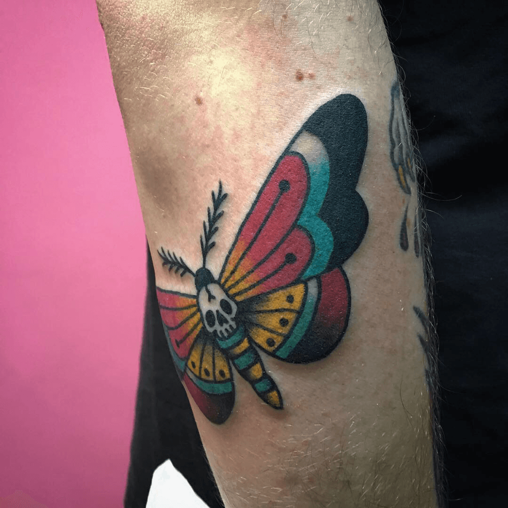Traditionele mot tattoo met een doodskop op het lijfje op de bovenarm.