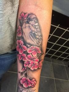 Mus op tak met roze kersenbloesem op onderarm.