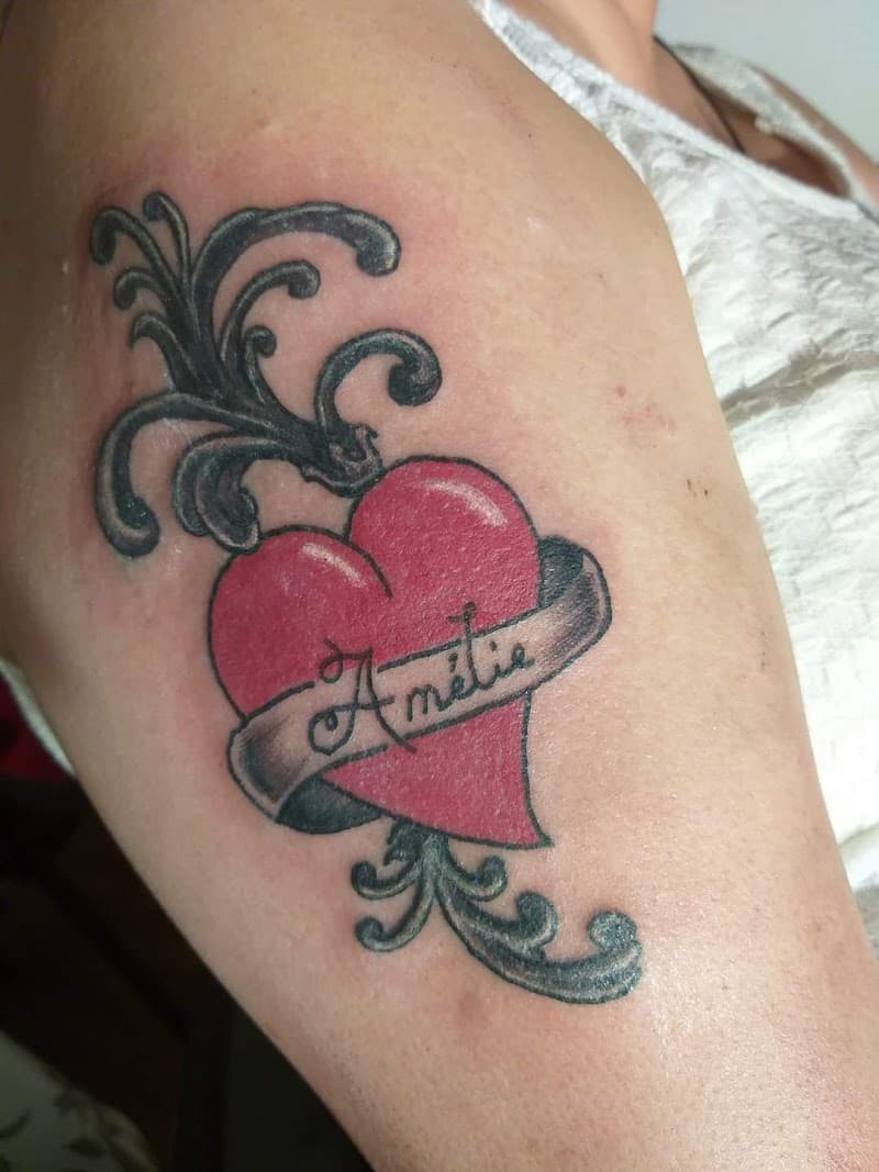 Rood hart met banner 'Amélie' en zwarte sierkrullen op bovenarm.