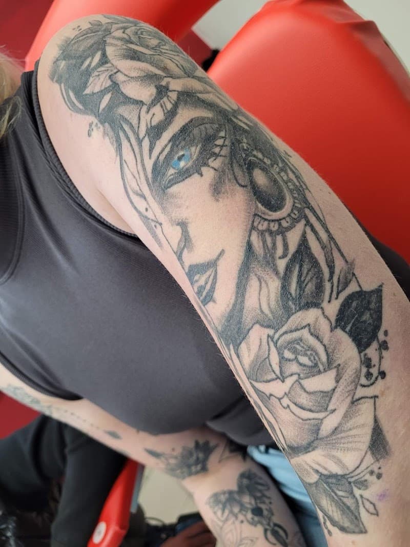 Zwart-wit tattoo van een vrouwenportret met een roos op de bovenarm.