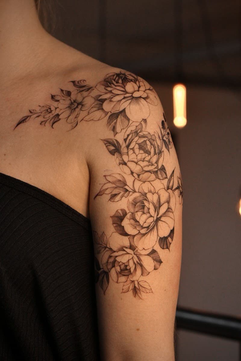 Fineline bloemen tattoo op schouder en bovenarm.