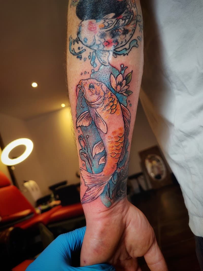Kleurrijke koi karper tattoo met water en lotus op onderarm.