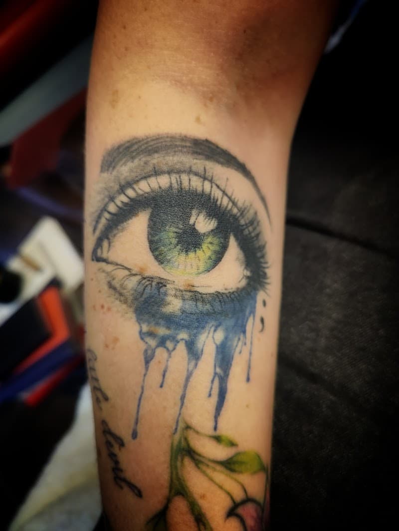 Realistisch oog met blauwe aquarel tranen en tekst op de onderarm.