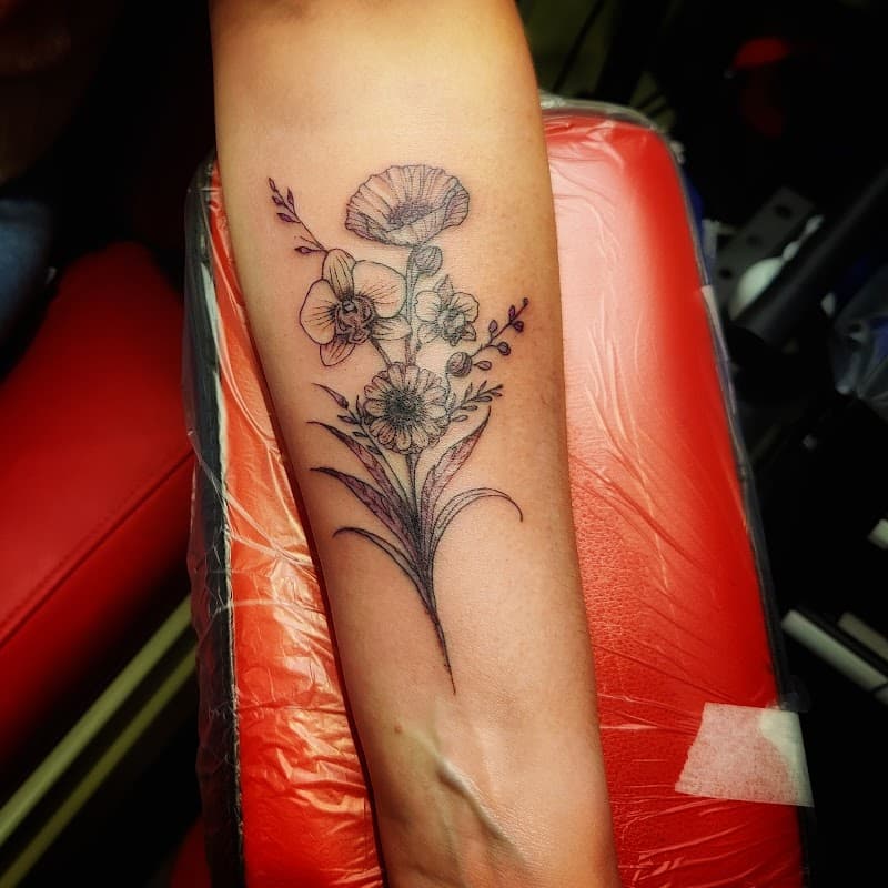 Fineline bloemenboeket met orchidee en klaproos op onderarm.