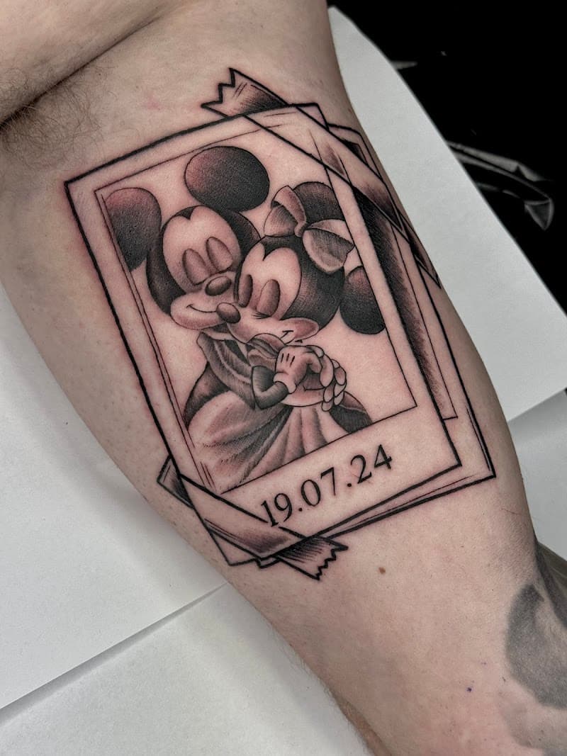 Zwart-wit tattoo van Mickey en Minnie Mouse in een polaroid met datum.