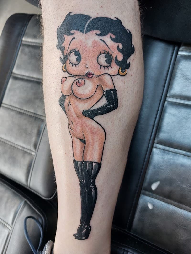 Close-up van een kleuren tattoo van een naakte Betty Boop op het onderbeen.