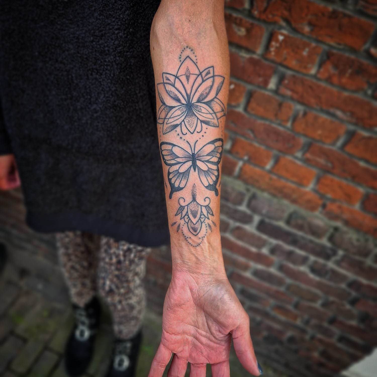 Dotwork lotus en vlinder tattoo op onderarm.