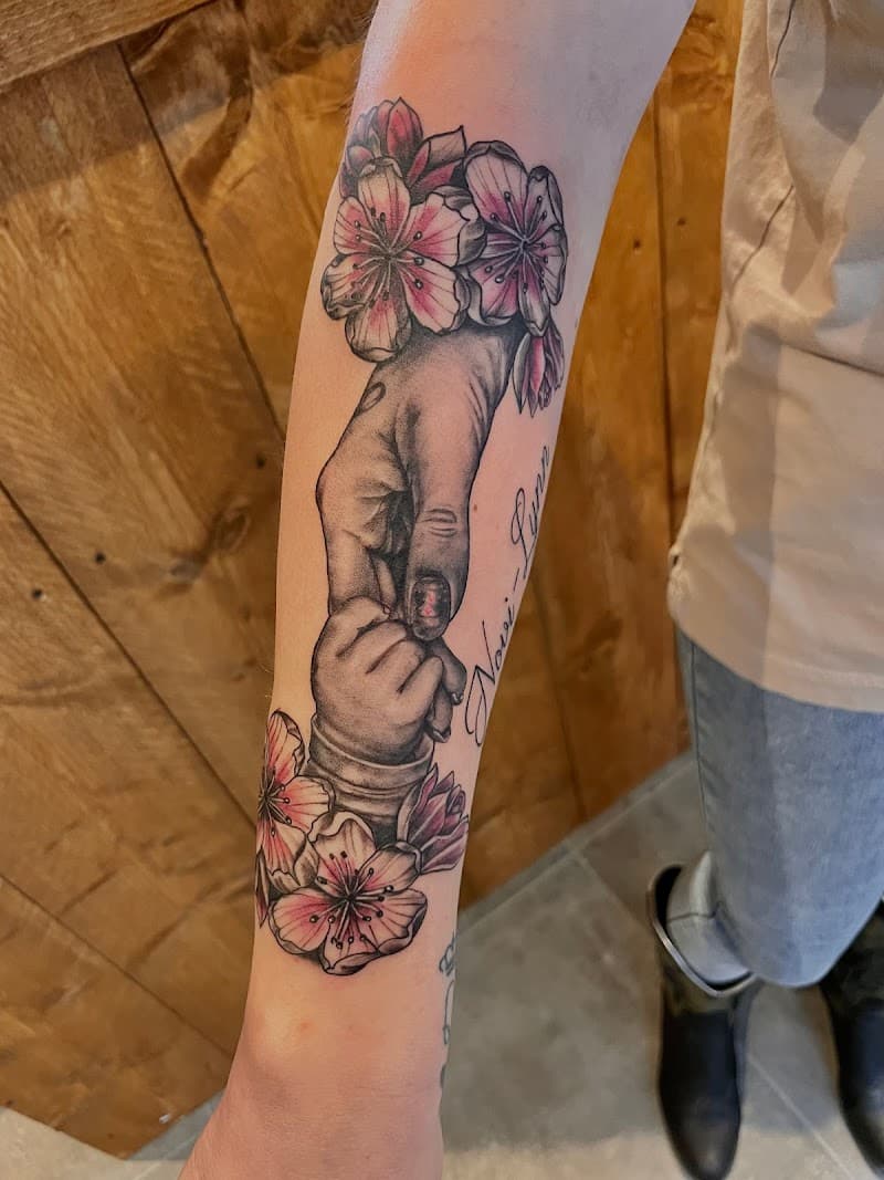 Realistische tattoo van een volwassen hand die een babyhandje vasthoudt, met kersenbloesem en naam.