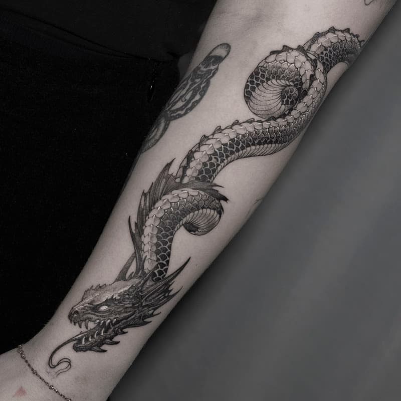 Gedetailleerde zwart-wit draak tattoo die kronkelt over de onderarm.
