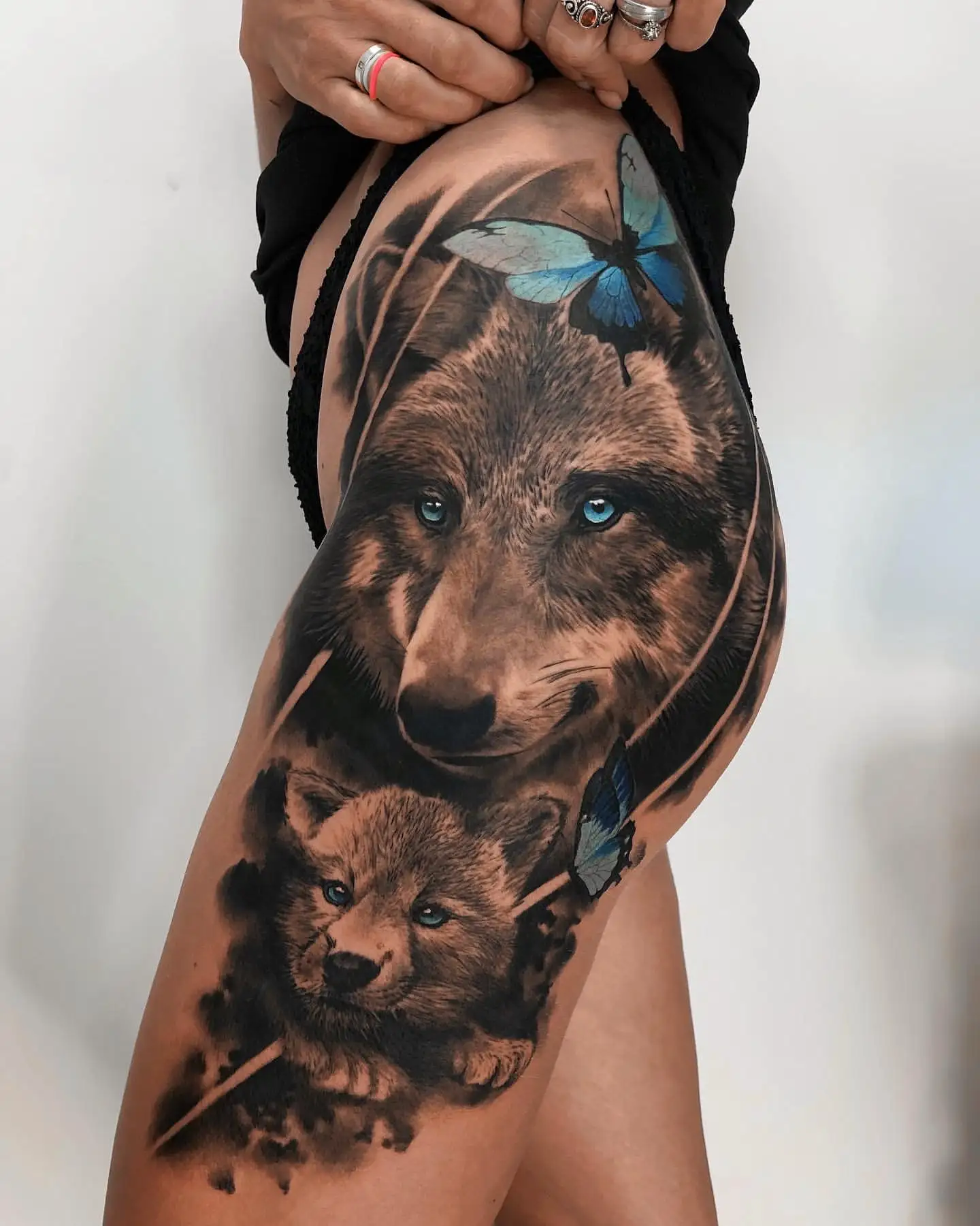 Realistische wolf en welp met blauwe vlinders op bovenbeen.