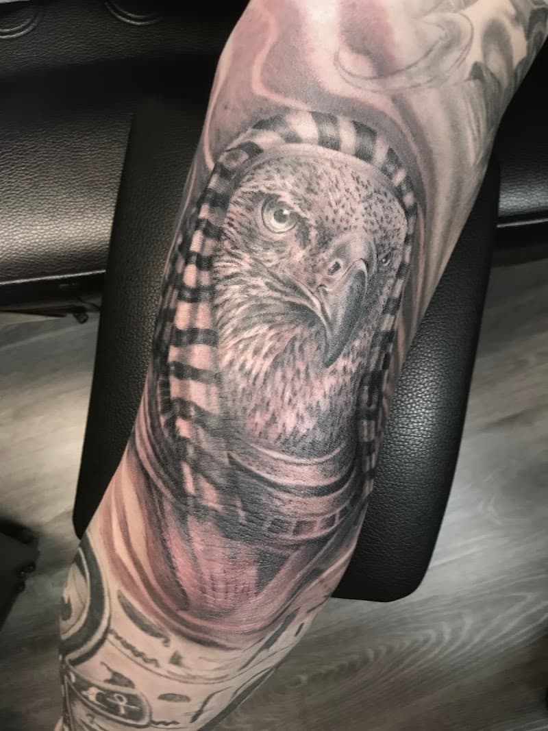 Zwart-wit tattoo van een valk met Egyptische hoofdtooi op de bovenarm.