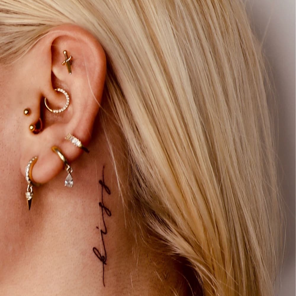 Fineline tekst tattoo 'kiss' achter het oor.