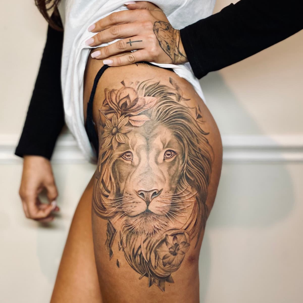 Grote realistische leeuwenkop met bloemen op bovenbeen.