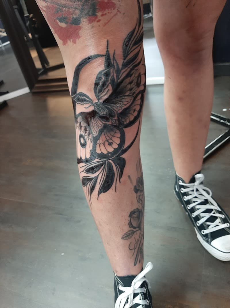 Grote blackwork vlinder/mot met bladeren op het onderbeen.