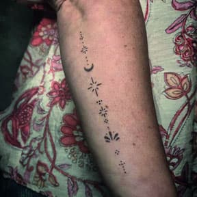 Minimalistische fineline tattoo met maan, sterren en stippen op onderarm.