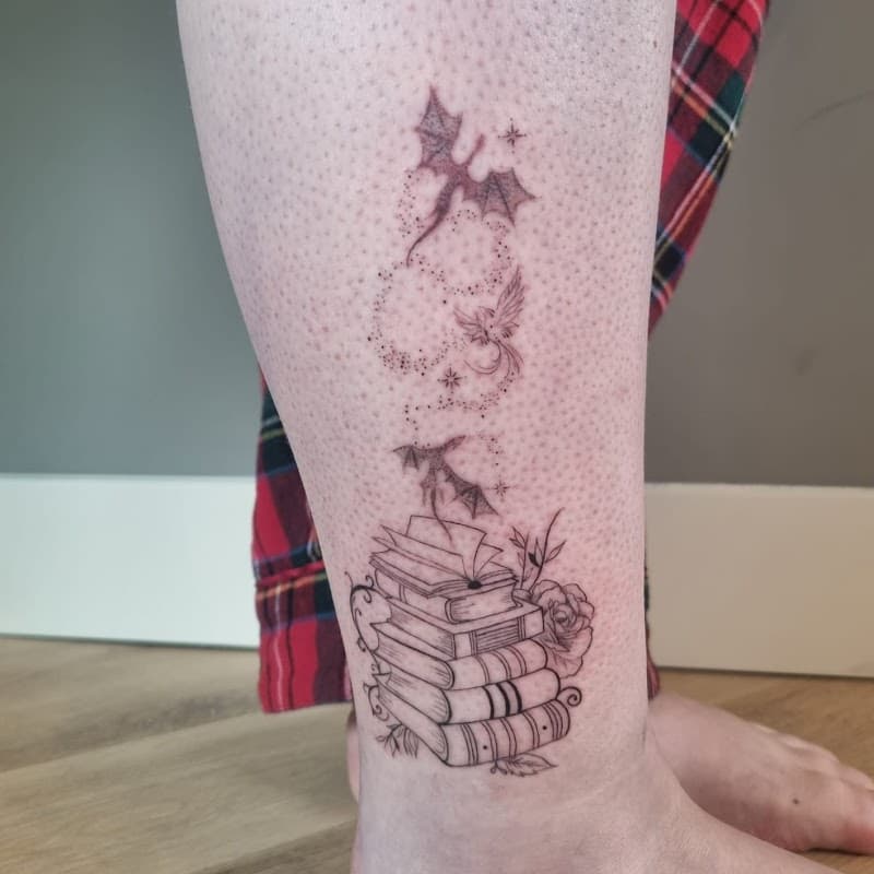Fineline tattoo van een stapel boeken met draken en een feniks die eruit vliegen.
