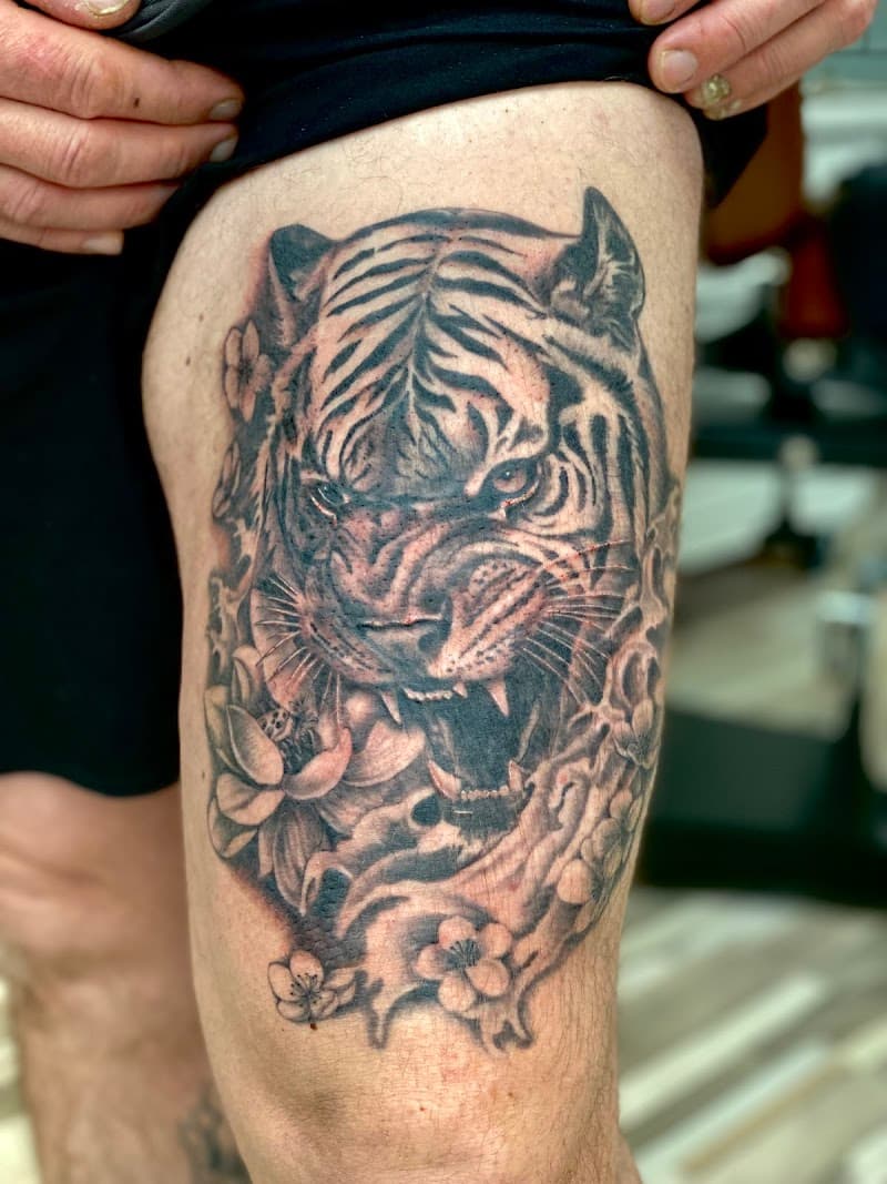 Realistische tijgerkop met bloemen op bovenbeen.