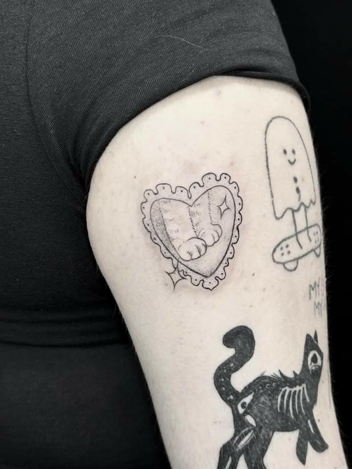 Fineline tattoo van kattenpootjes in een hartvormig kader op de bovenarm.