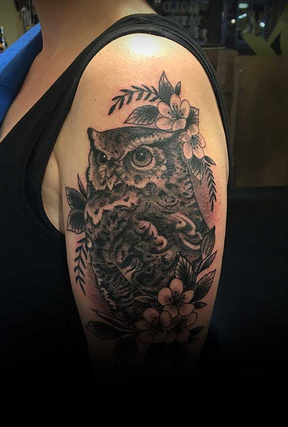 Zwart-wit uil met bloemen en bladeren op de bovenarm.