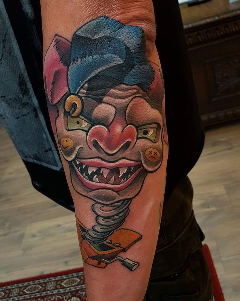 Kleurrijke neo-traditional jack-in-the-box clown tattoo op onderarm.