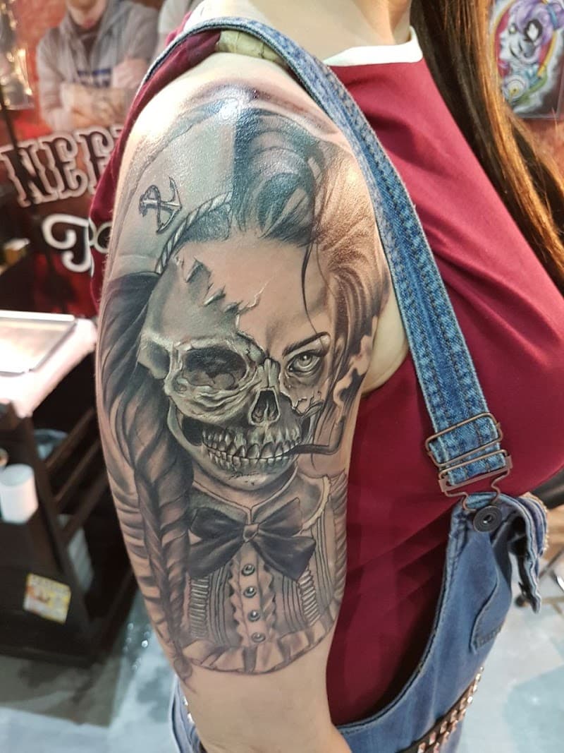 Zwart-wit tattoo van een vrouw met een half schedelgezicht en een matrozenpet.