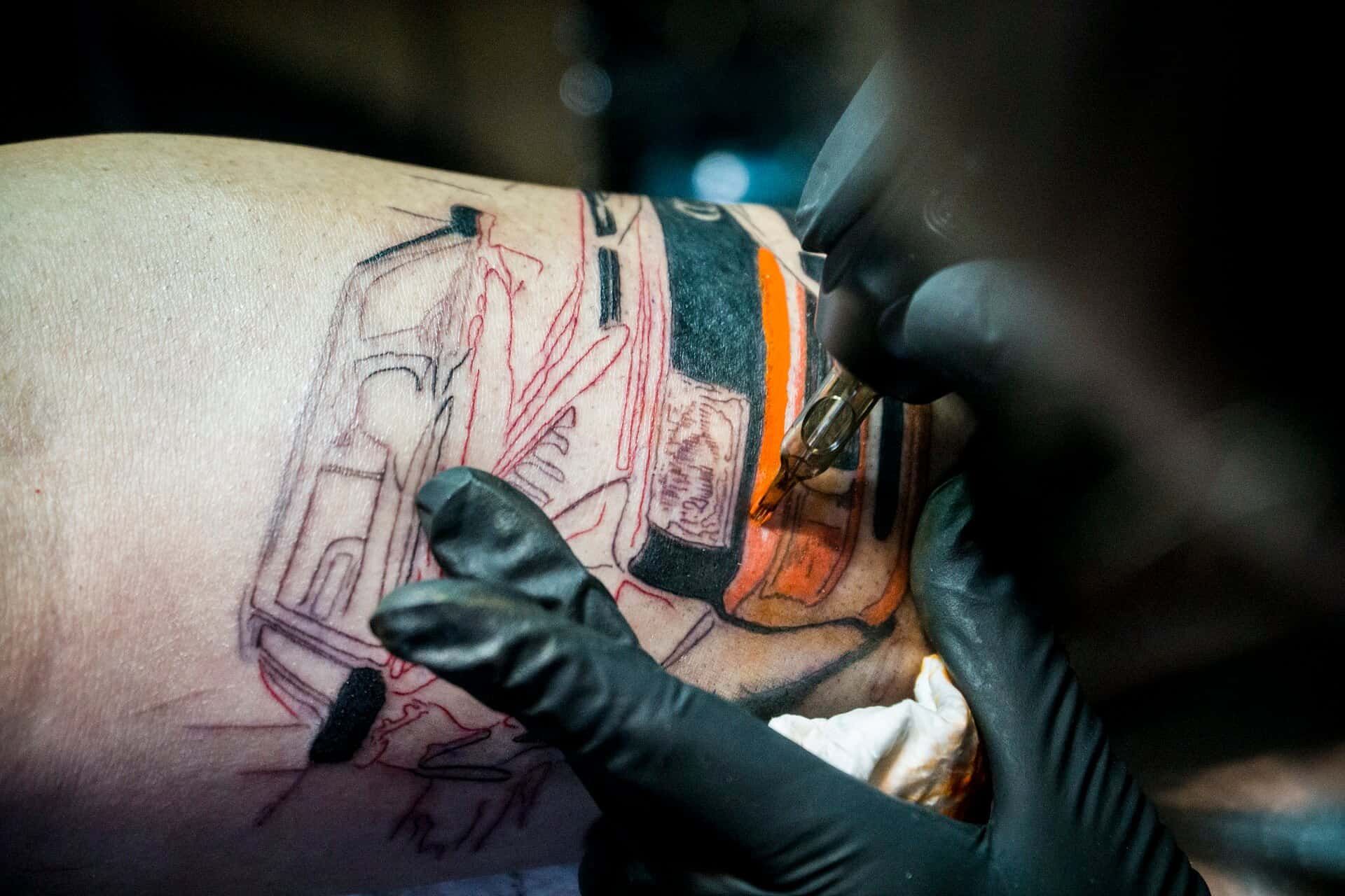 Close-up van een tattoo van een voertuig in wording, met oranje en zwarte inkt.