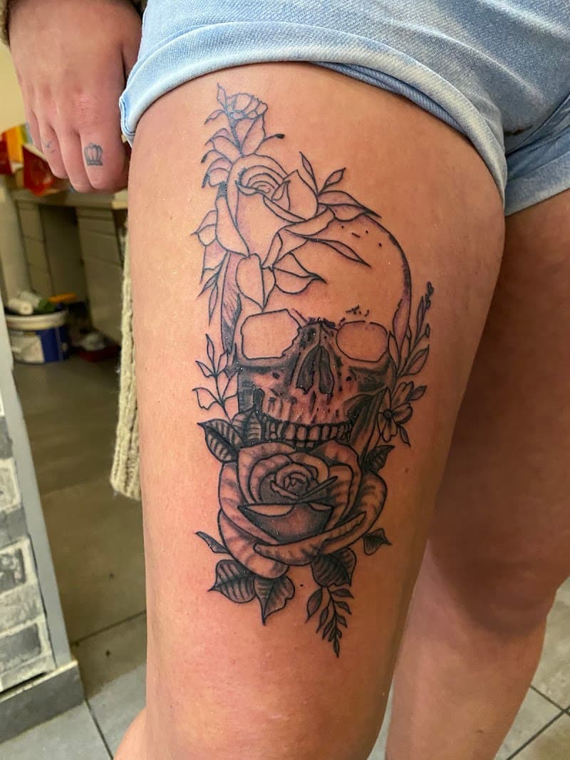 Illustratieve tattoo van een schedel met rozen op het bovenbeen.