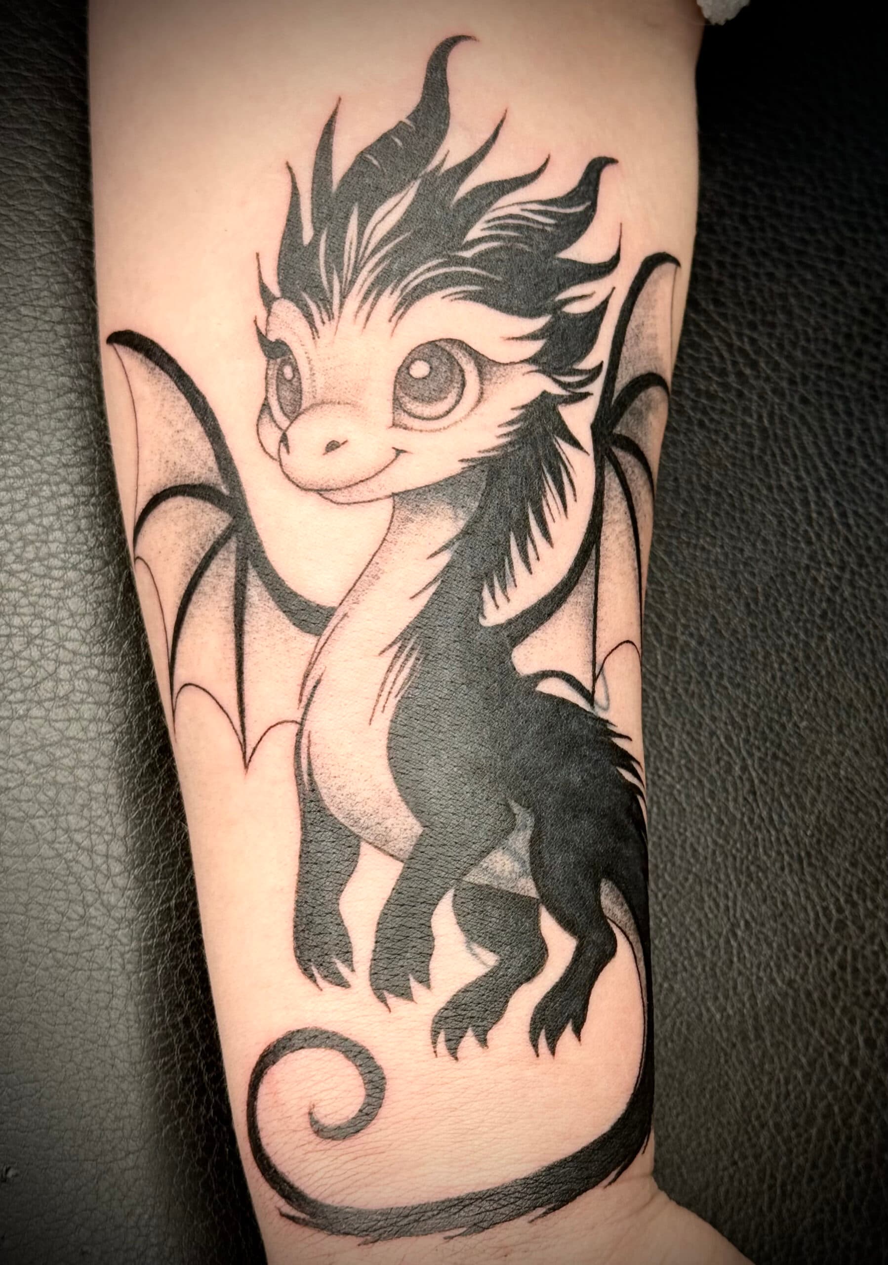 Schattige baby draak tattoo in blackwork stijl op de onderarm.