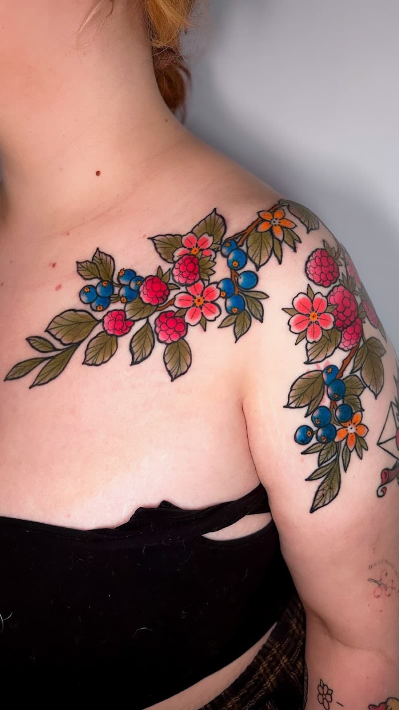 Kleurrijke tattoo van een tak met frambozen, blauwe bessen en bloemen op schouder.
