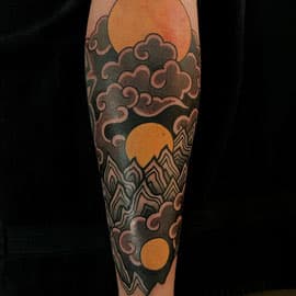 Japanse stijl tattoo van wolken, bergen en drie zonnen op het onderbeen.