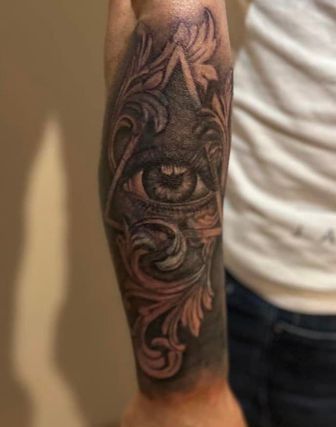 Zwart-wit oog in driehoek met barokke versieringen op onderarm.