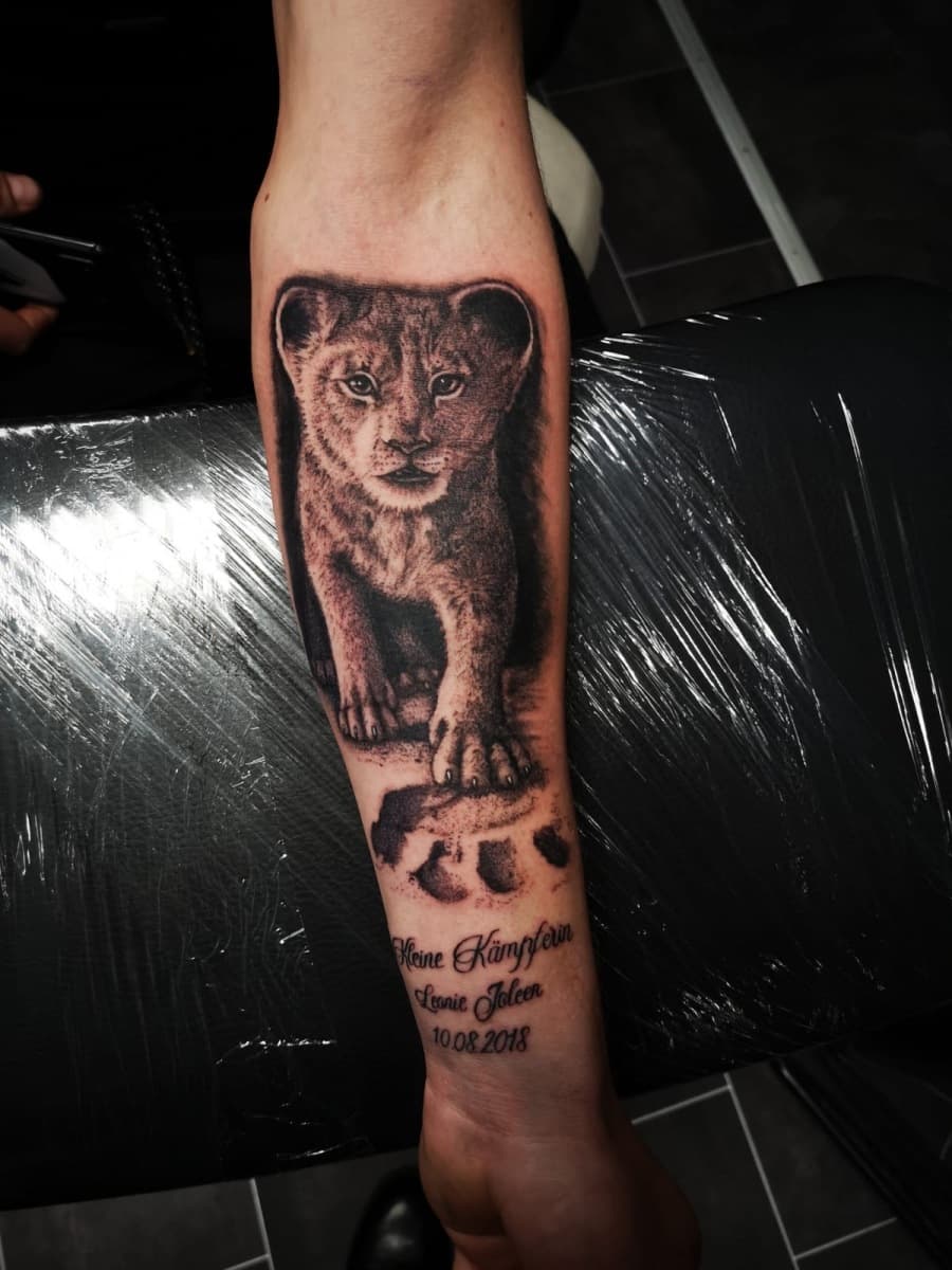 Realistische leeuwenwelp met pootafdruk en tekst op onderarm.