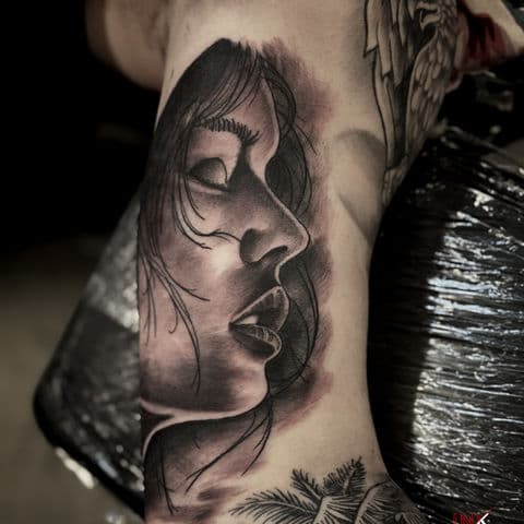 Realistisch zwart-wit portret van een vrouwen gezicht in profiel op de bovenarm.