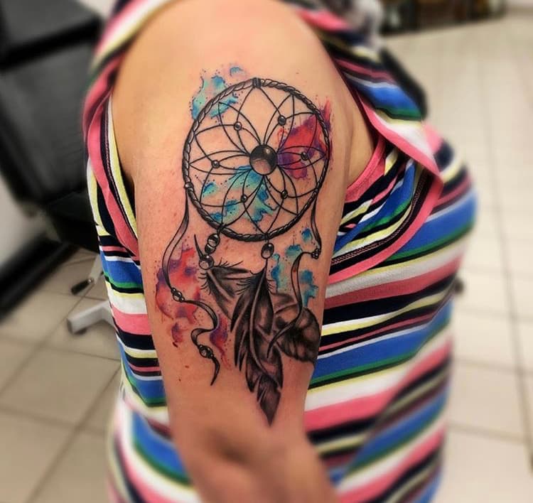 Dromenvanger tattoo met veren en aquarel achtergrond op bovenarm.