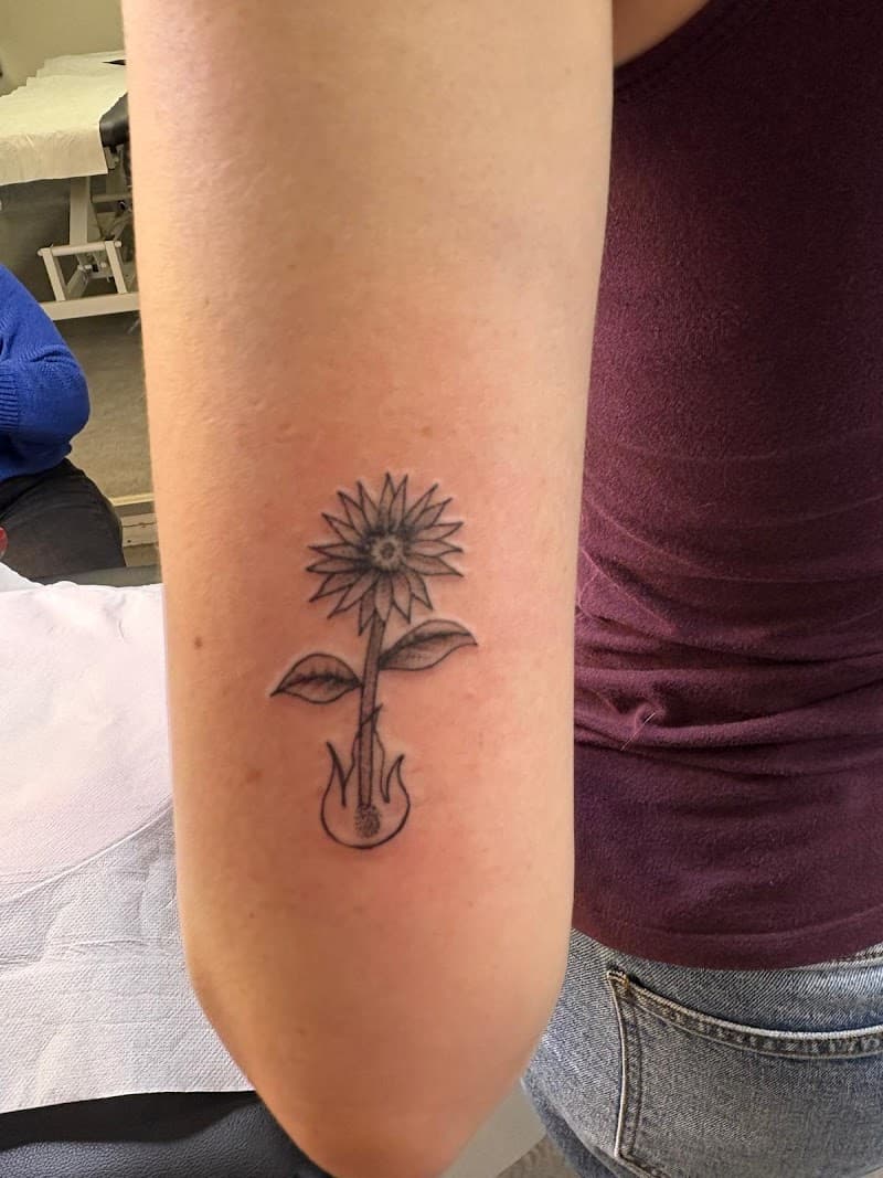 Fineline tattoo: zonnebloem groeit uit vlam op de achterkant van de bovenarm.