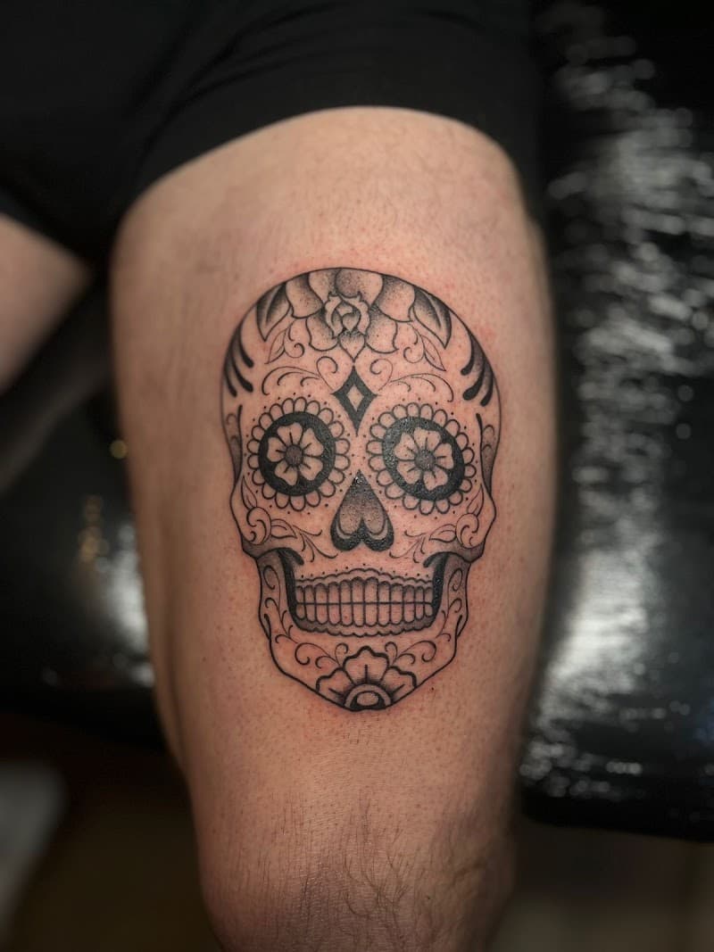 Blackwork sugar skull tattoo met bloemmotieven op bovenbeen.