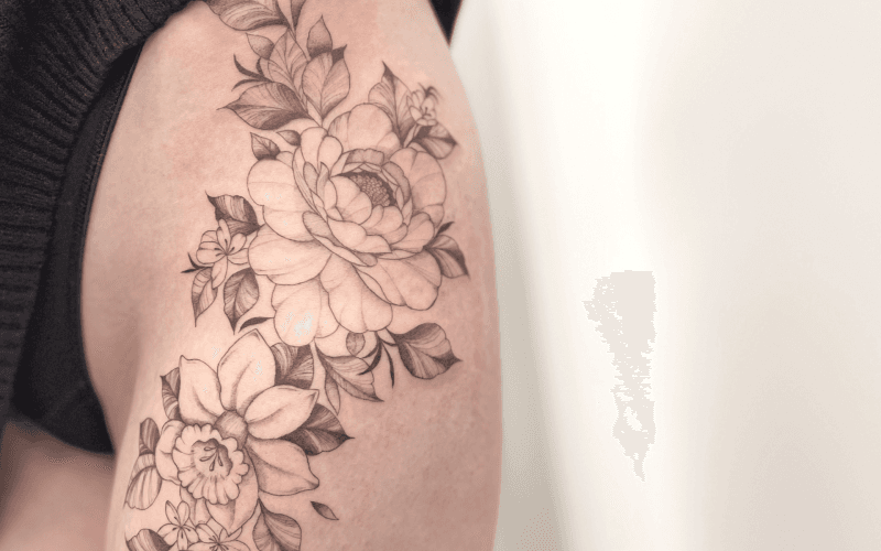 Fineline bloemen tattoo op bovenbeen, pioenroos en narcis.