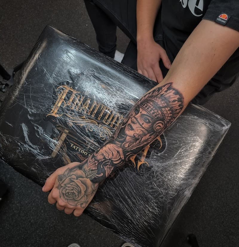 Zwart-wit tattoo van een inheemse vrouw met verentooi en een roos op de hand.